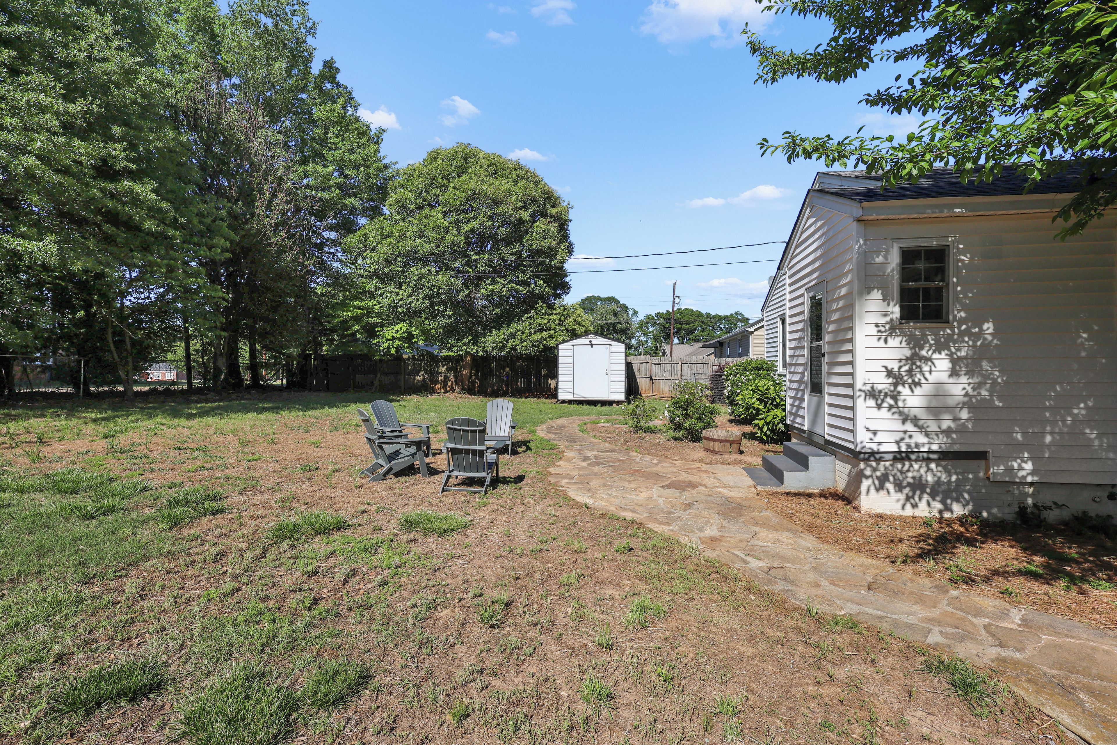 A backyard with a stone patio, a small shed, and a white house.