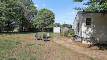 A backyard with a stone patio, a small shed, and a white house.