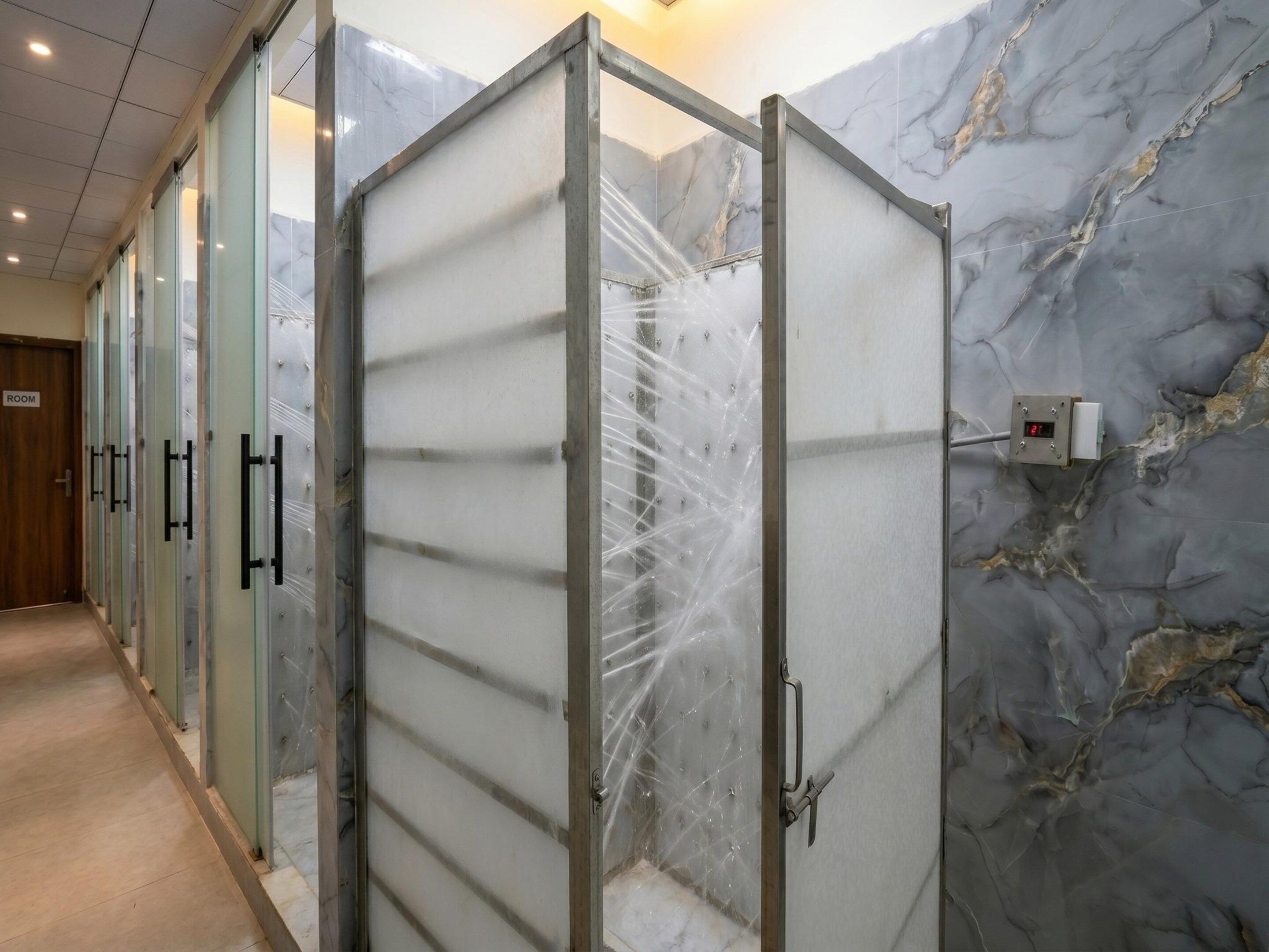 A hallway with a row of glass-enclosed shower cubicles, marble walls, and a digital display.