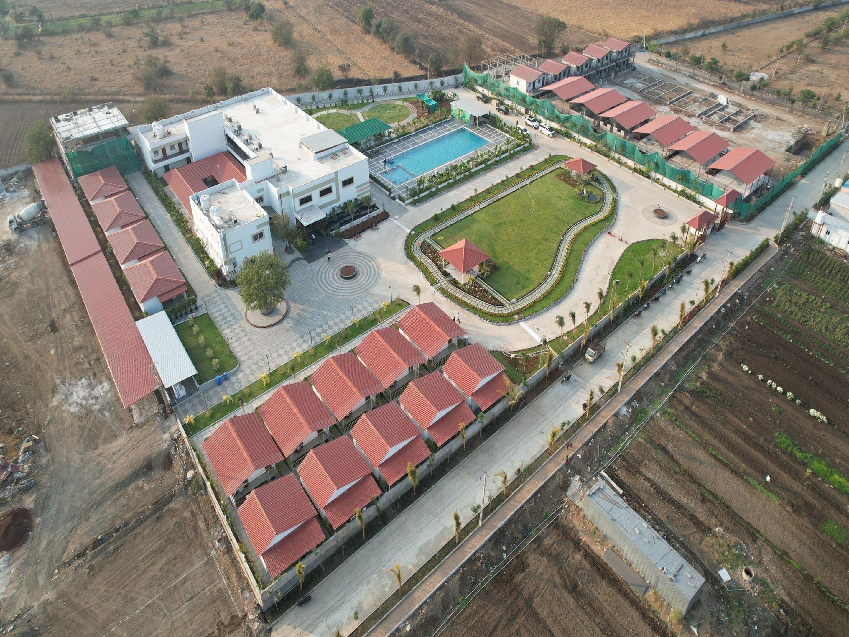 An aerial view of a residential complex with multiple buildings, a swimming pool, and landscaped gardens.
