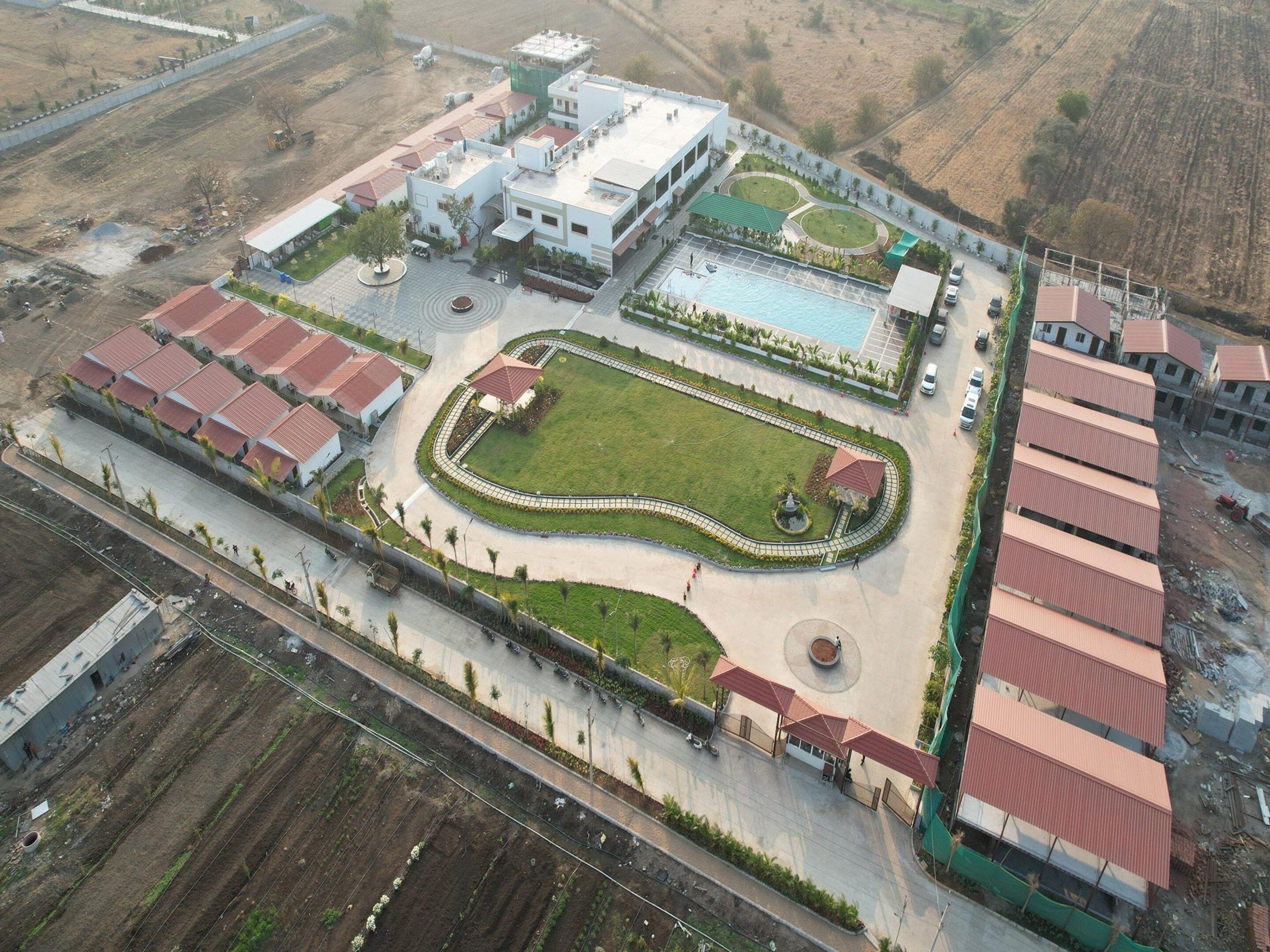 An aerial view of a residential complex with multiple buildings, a swimming pool, and landscaped areas.