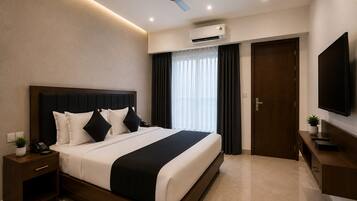A modern hotel room with a large bed, a ceiling fan, an air conditioning unit, a television, and a small plant.