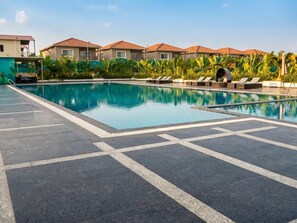 Piscina com espreguiçadeiras e área coberta, rodeada por edifícios com telhados vermelhos.