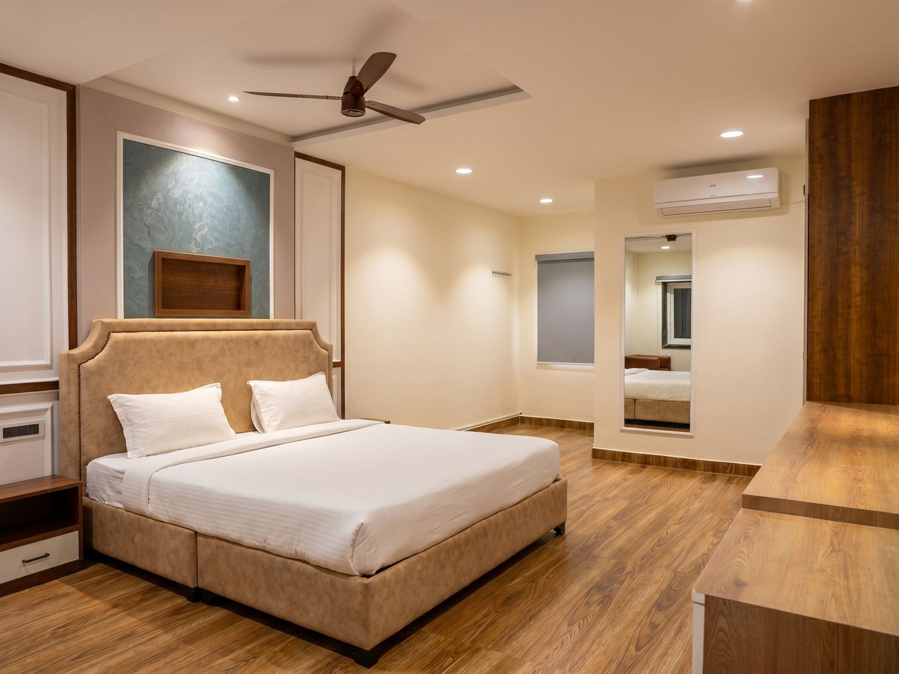 Un dormitorio con una cama grande, ventilador de techo, equipo de aire acondicionado y piso de madera.