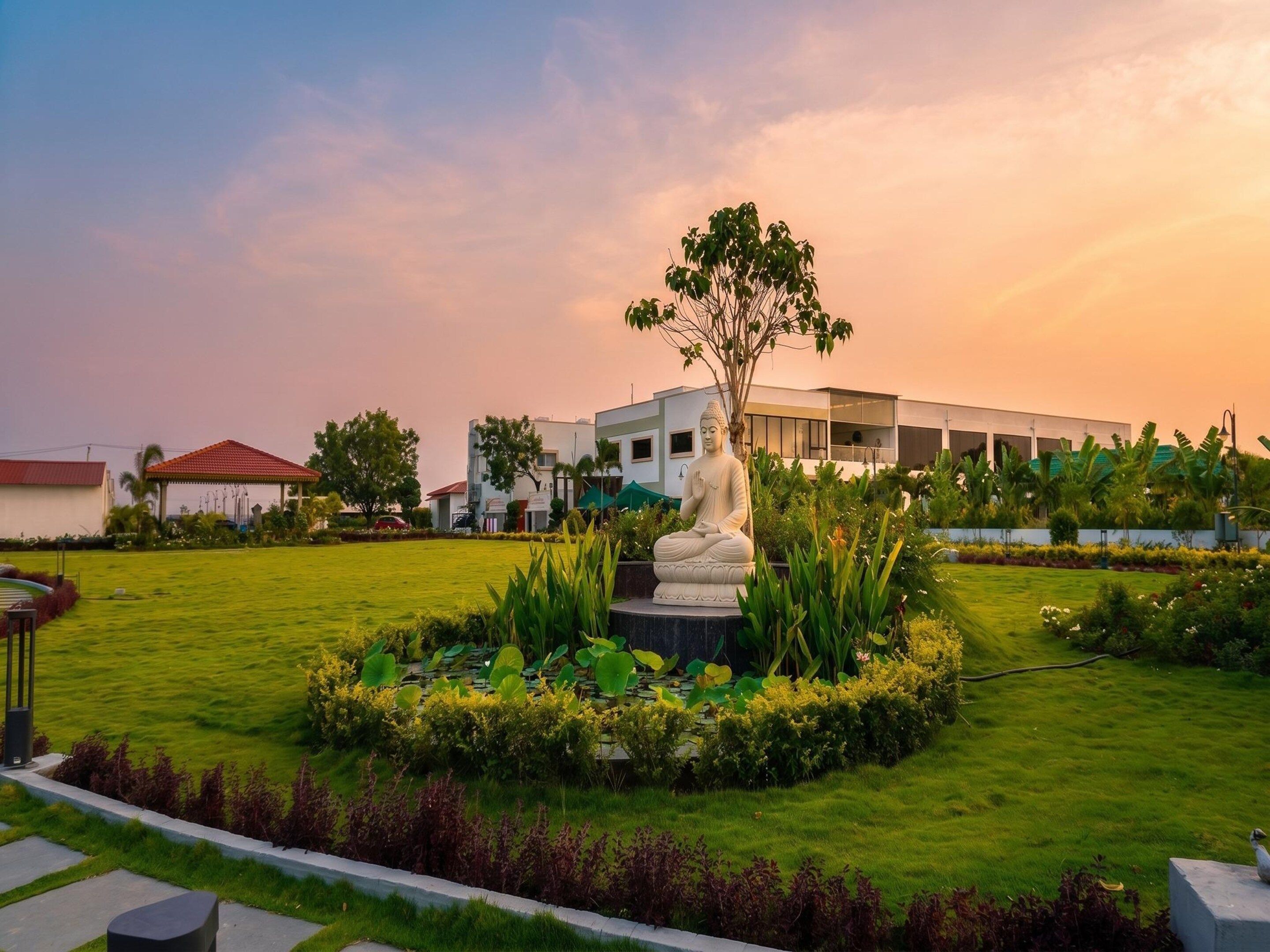 A serene garden with a Buddha statue, lush greenery, and a modern building in the background.