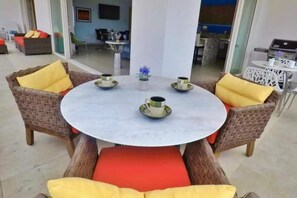A round table with four chairs, each with a cushion, and a vase with flowers in the center. - Zenith Penthouse 702 | Rooftop Pool & Ocean Views (Puerto Vallarta)