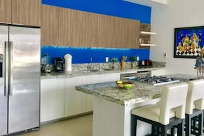 A modern kitchen with a stainless steel refrigerator, granite countertops, a gas stove, and a blue accent wall. - Zenith Penthouse 702 | Rooftop Pool & Ocean Views (Puerto Vallarta)