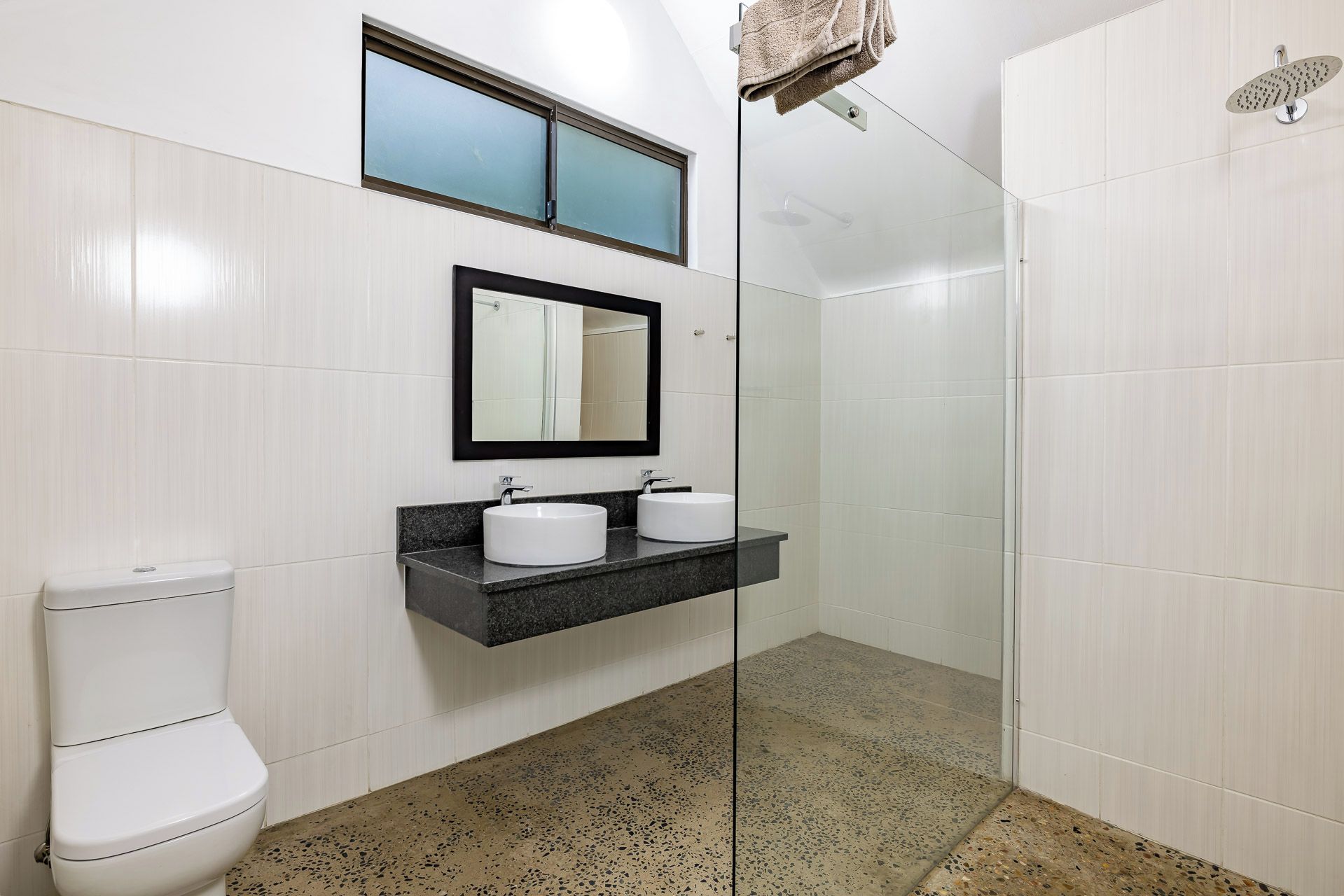 A bathroom with a toilet, two sinks, a mirror, and a shower.