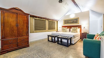 A bedroom with a large wooden wardrobe, a bed with floral pillows, a green armchair, and a small table.