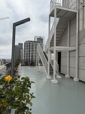 En takterrass med en trappa, planterade blommor och utsikt över de omgivande byggnaderna.