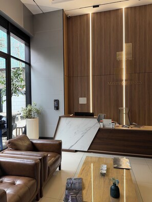 A modern reception area with a wooden reception desk, a marble wall, and a leather sofa. - Stylish One-Bedroom Stay Near GTC Westlands (Nairobi)