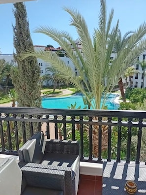 Ein Balkon mit Blick auf einen Swimmingpool, Palmen und ein Gebäude im Hintergrund.