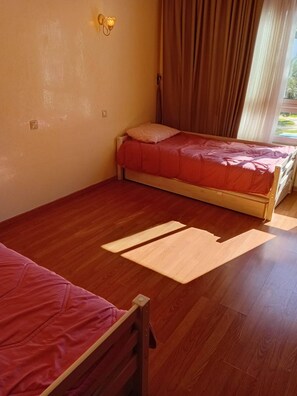 Ein Zimmer mit zwei Betten, Holzboden und einem Vorhangfenster.