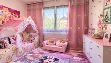 Een kamer voor kinderen, ingericht in roze tinten, met een bed, een roze bank, een dressoir en een raam met gordijnen.