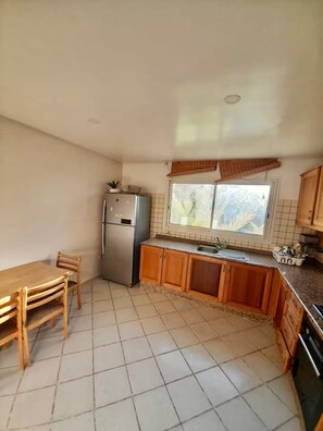 Eine Küche mit Kühlschrank, Holzschränken, einem Fenster und einem Fliesenboden.