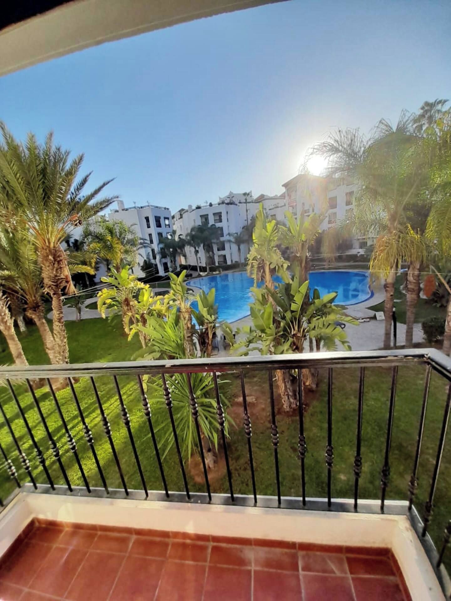 A balcony with a view of a swimming pool, surrounded by palm trees and buildings.