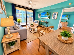 Una sala moderna con sofá, mesa de centro y mesa de comedor, un balcón con vistas y decoración de temática tropical.