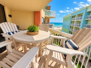 Une terrasse en bois avec une table ronde et des chaises, une petite plante en pot et une vue sur la plage et l’océan.