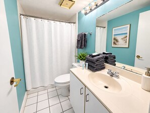 Une salle de bain avec des toilettes blanches, un lavabo avec un miroir et un rideau de douche.