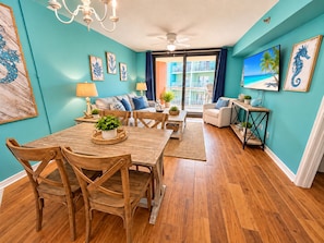 A modern living room with a dining area, featuring a wooden table and chairs, a sofa set, and a balcony with a view. - Cute 2 Bed 2 Bath at Harbor Place - Fall Specials! (Orange Beach)