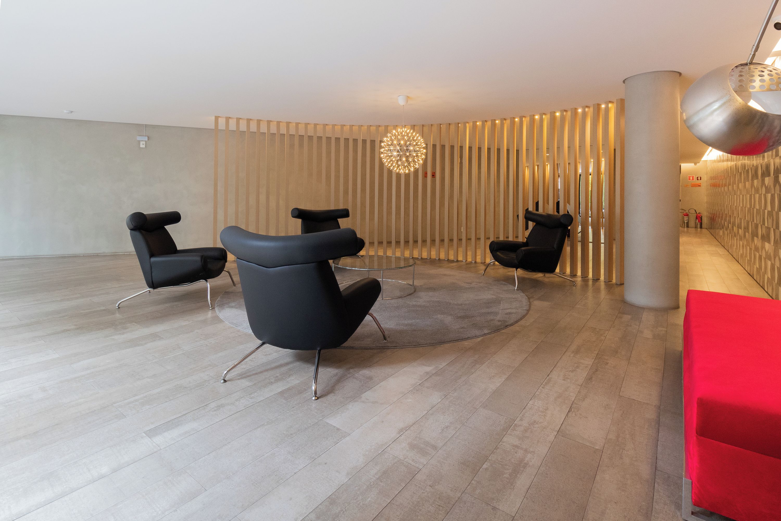 Un interno moderno con tre sedie nere, un tavolo rotondo in vetro e un lampadario originale.