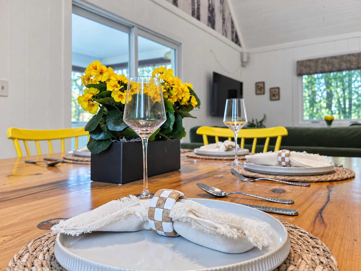 Una mesa de comedor dispuesta con platos, cubiertos y un centro de mesa de flores amarillas.