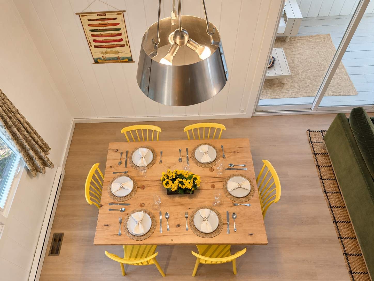 Een eetruimte met een houten tafel voor zes personen, gele stoelen en een hangende lamp.