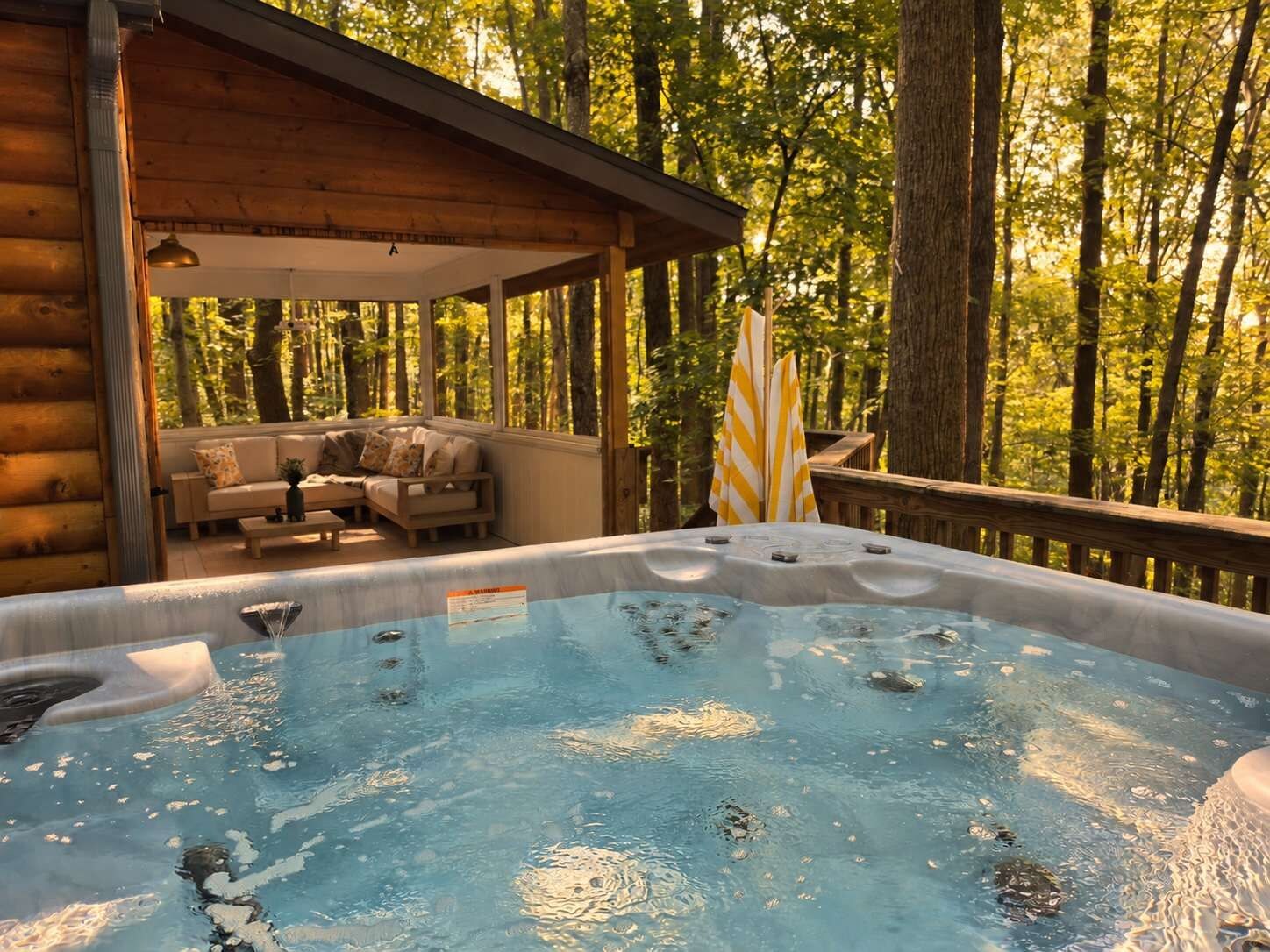 Un jacuzzi con cubierta de madera y un sofá, rodeado de árboles.