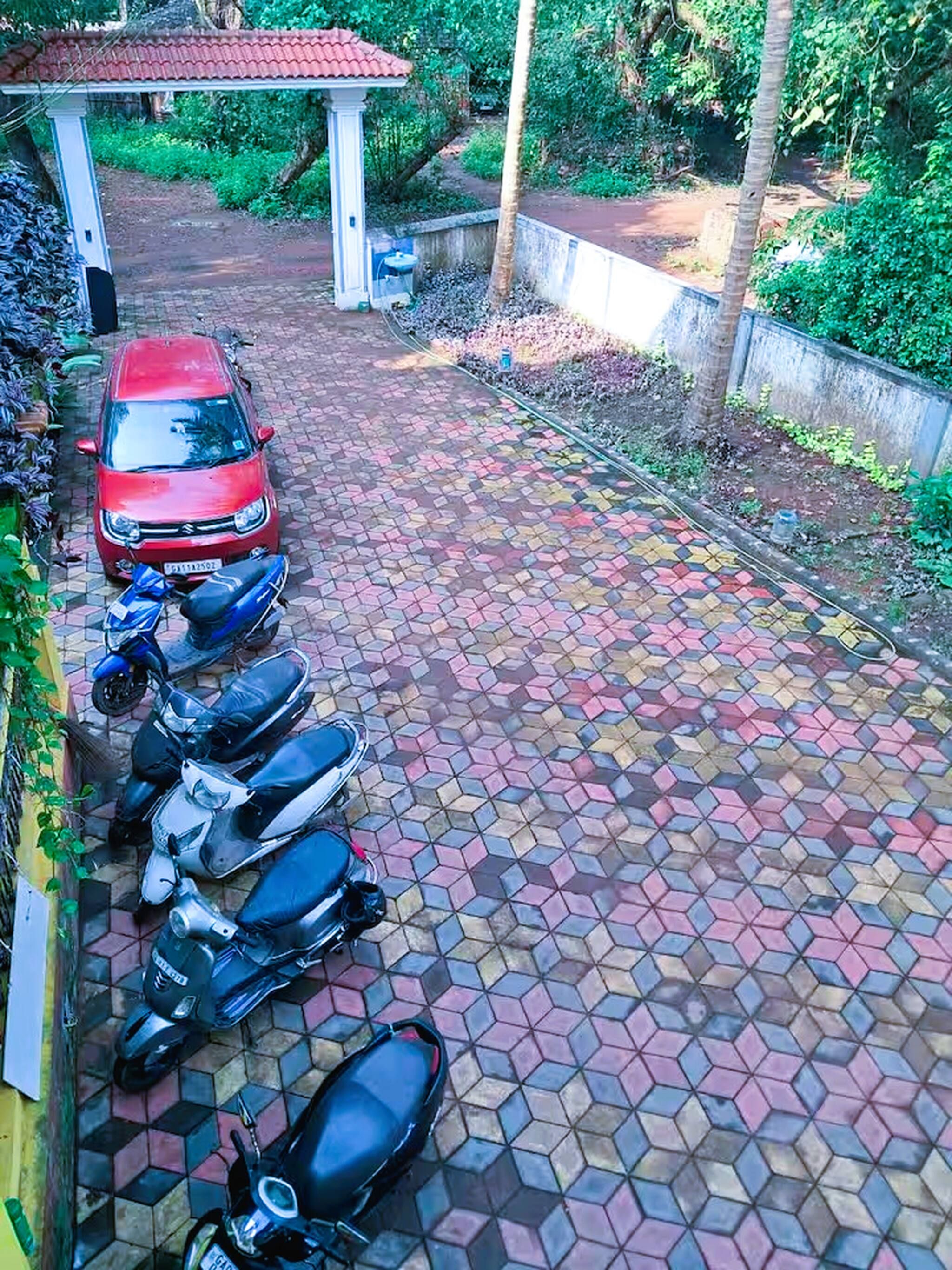 Asfaltoitu ajotie, jonka varrella on punainen auto ja useita parkkeerattuja skootteria.