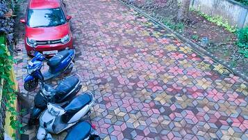 Un camino de entrada pavimentado con un coche rojo y varias scooters estacionadas.