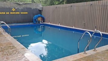 A swimming pool with a wooden fence and a sign that reads 'FARM DE MUKUND SADAN'.