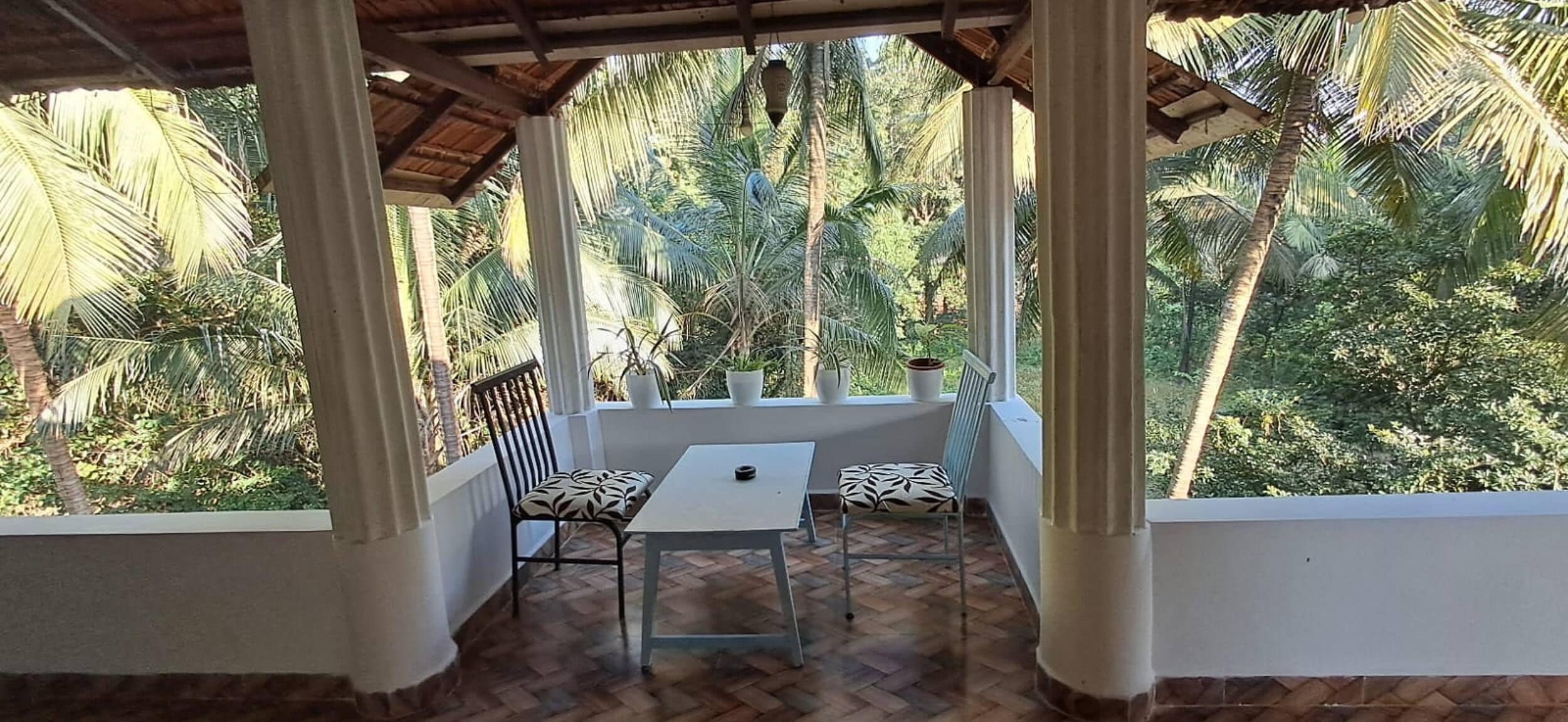 Un espacio de estar al aire libre cubierto con una mesa y dos sillas, rodeado de exuberante vegetación tropical.