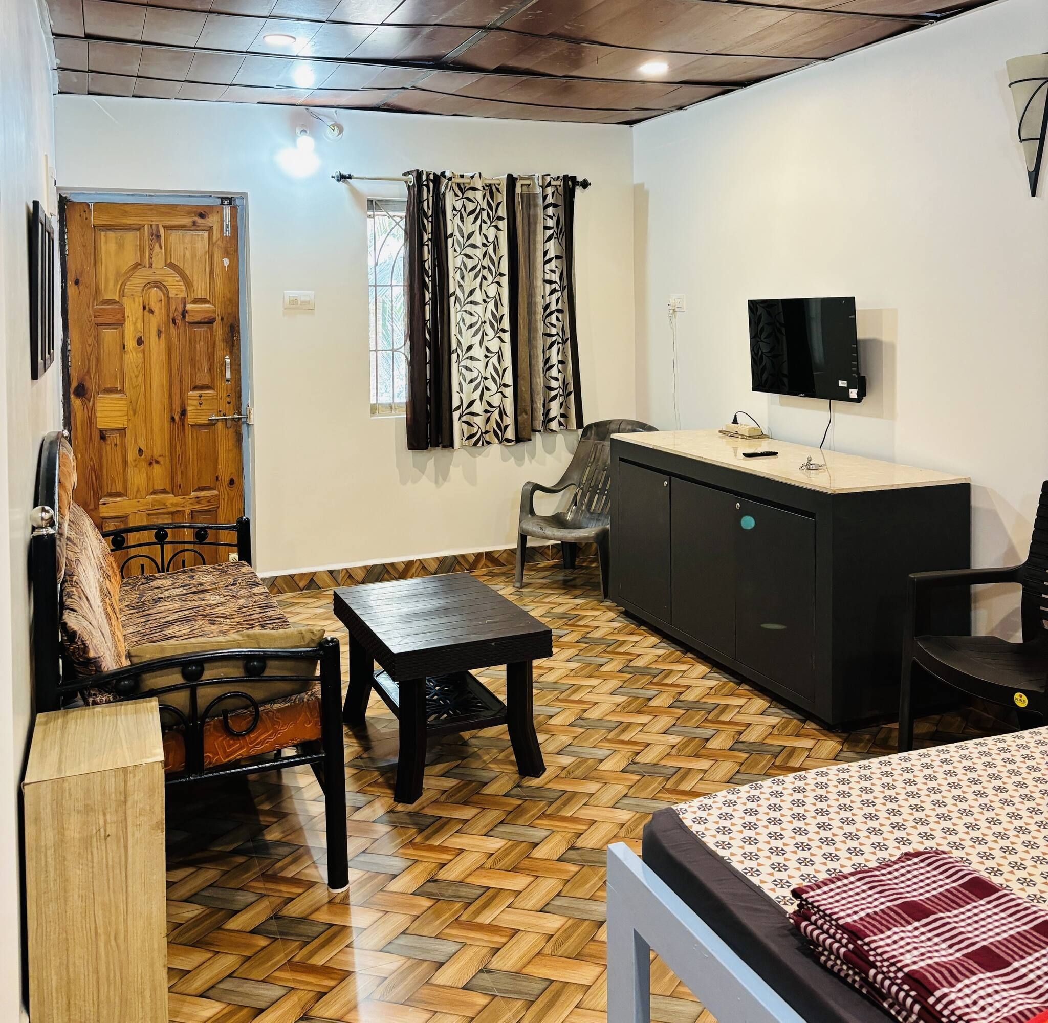 A room with a wooden door, a sofa, a dining table, a TV, and a patterned floor.