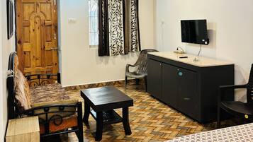 A room with a wooden door, a sofa, a dining table, a TV, and a patterned floor.