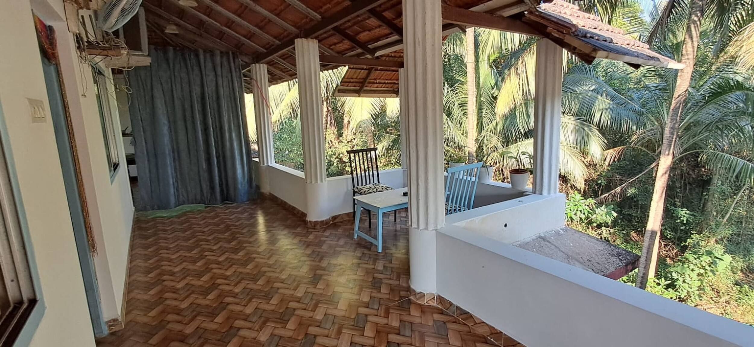 A covered outdoor area with a herringbone floor, a table with chairs, and a view of palm trees.