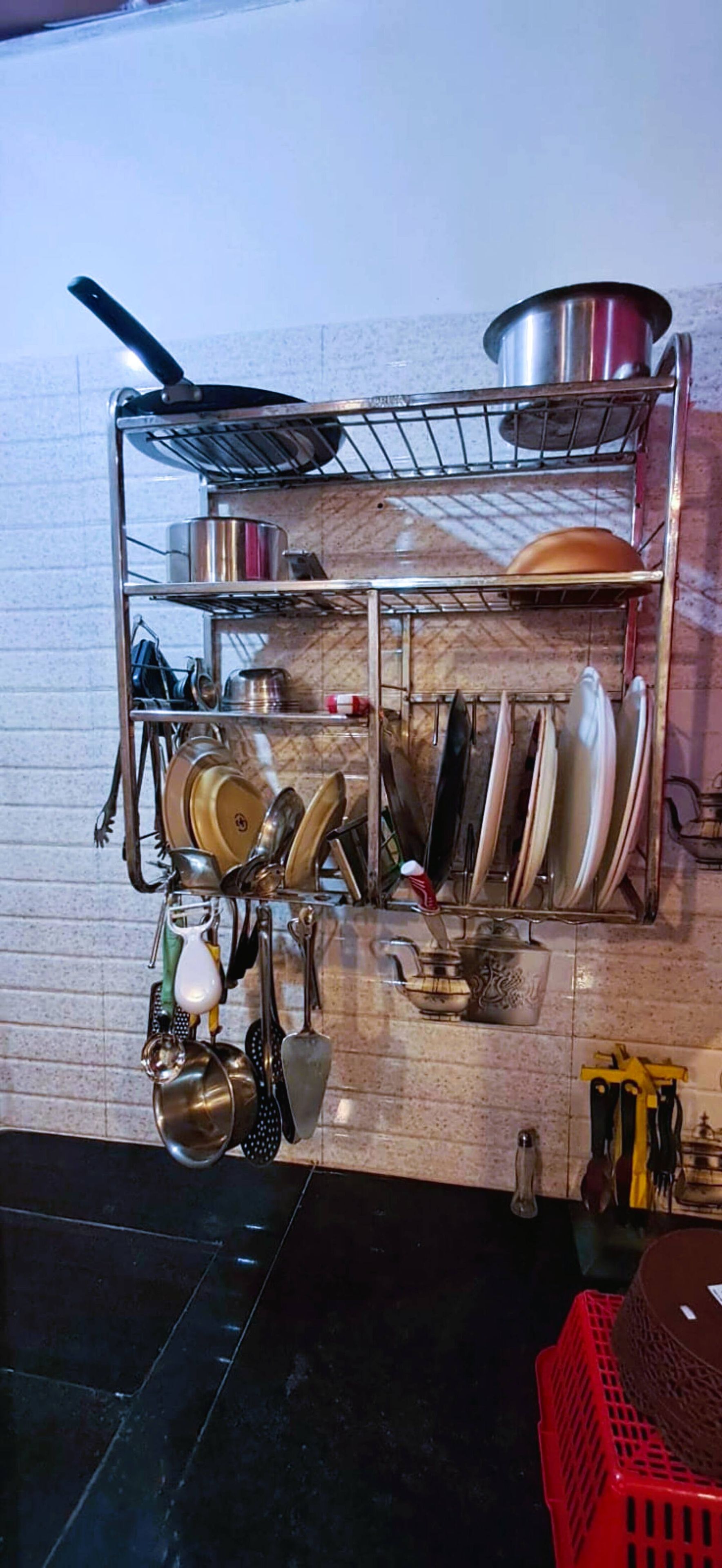 Una cocina con un estante metálico que contiene ollas, sartenes, una cesta roja y diversos utensilios de cocina.