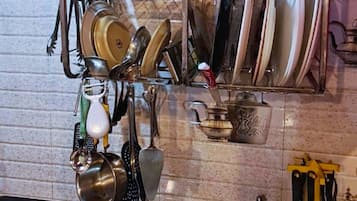 Una cocina con un estante metálico que contiene ollas, sartenes, una cesta roja y diversos utensilios de cocina.