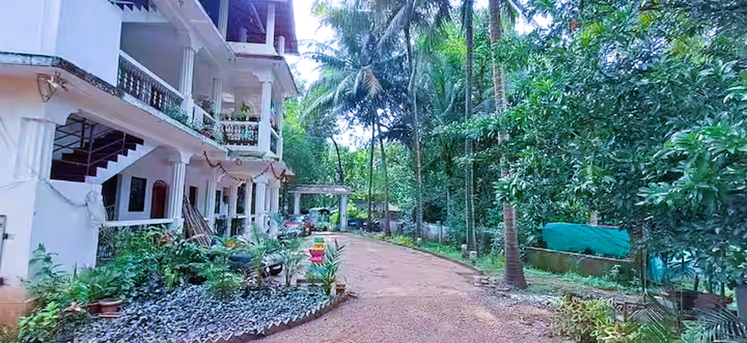 Um edifício residencial com varanda, escadaria e um jardim com diversas plantas.