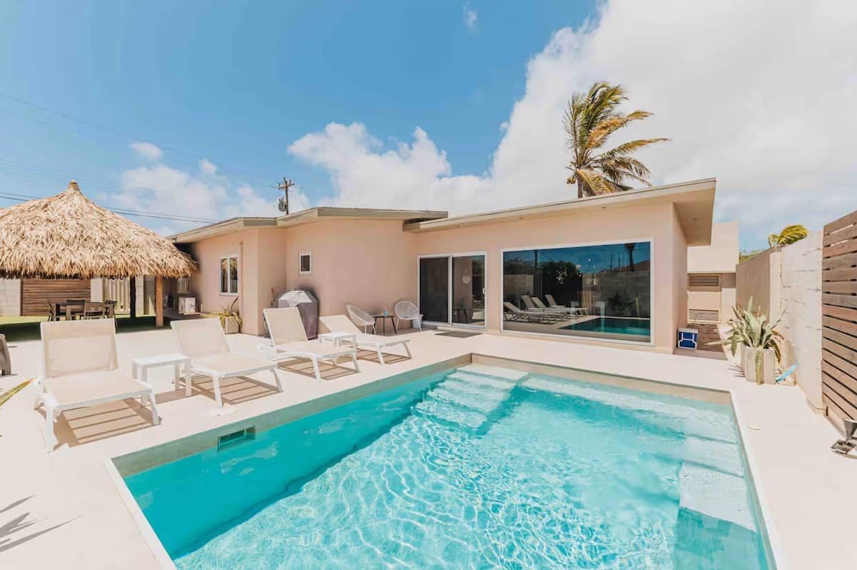 A modern house with a swimming pool, lounge chairs, and a thatched-roof structure.