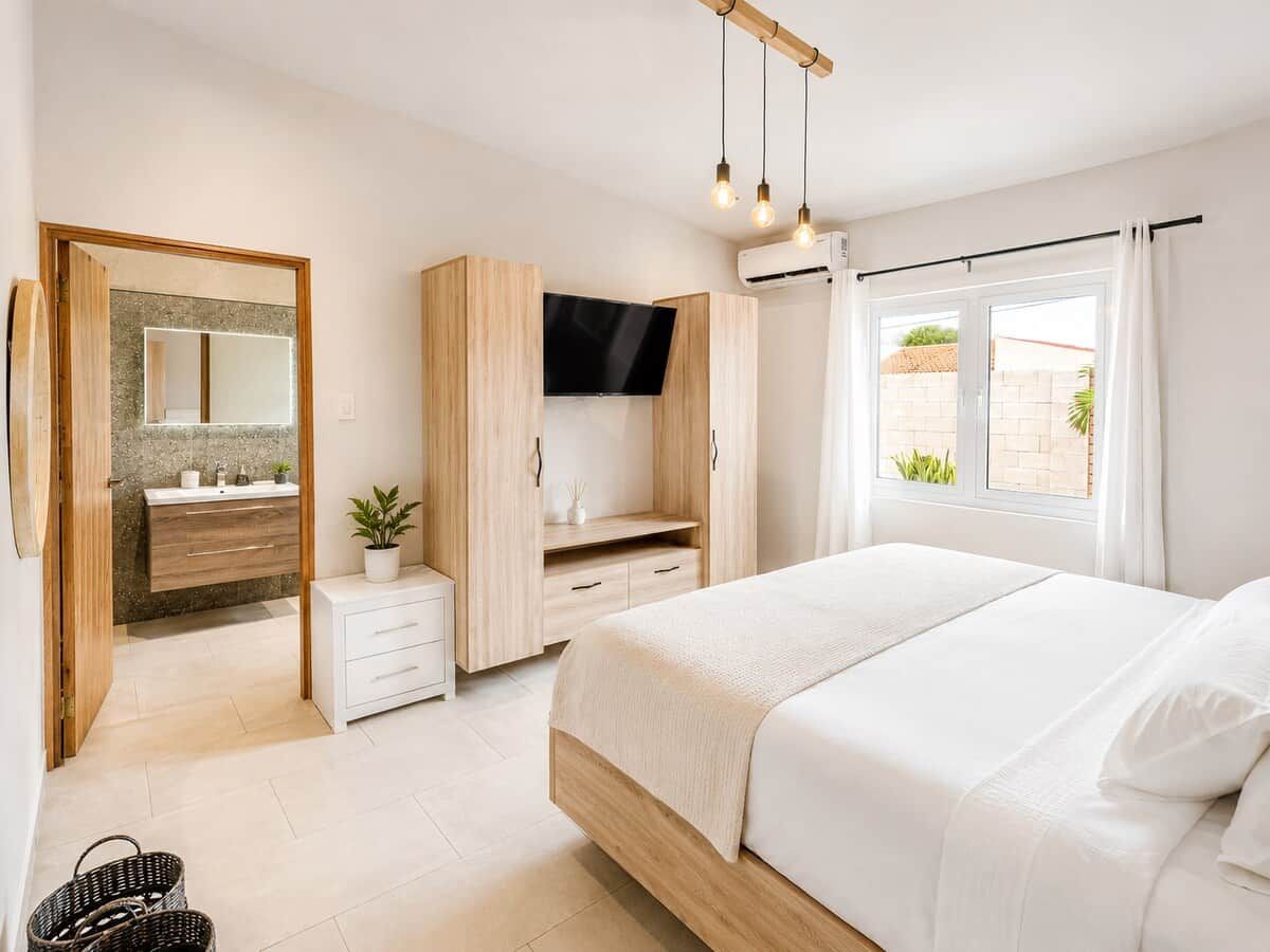 Un dormitorio con cama, televisor, armario y ventana con cortinas.