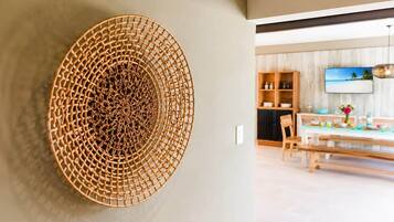 A modern interior with a circular woven light fixture on a wall, a dining area with a wooden table and chairs, and a television mounted on the wall.