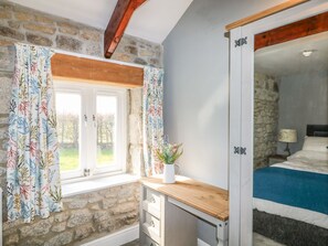 Ein Schlafzimmer mit einer Steinwand, einem Holztisch, einem Bett mit blauer Bettdecke und einem Fenster mit Vorhängen.
