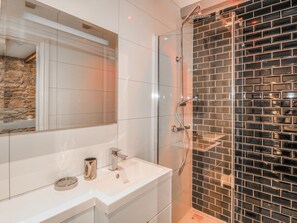 Ein modernes Badezimmer mit einer Duschkabine aus Glas, einem weißen Waschtisch mit Spiegel und einer gefliesten Rückwand.
