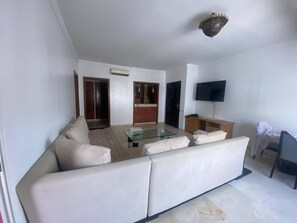 A living room with a sofa, a glass coffee table, a flat-screen TV, and a wooden cabinet. - Stylish Marina Apartment Steps from Beach (Agadir)