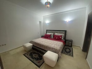A bedroom with a bed, two bedside tables, a nightstand, a rug, and a chair. - Stylish Marina Apartment Steps from Beach (Agadir)