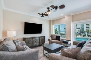 A living room with a flat-screen TV, a ceiling fan, and a view of a pool. - Lux Beach Getaway | Sleeps 28 | Beach Steps Away (Gulf Shores)