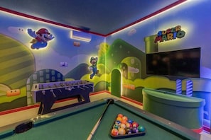 Una habitación con mesa de billar, mesa de fútbol de mesa y una pared temática de Super Mario.