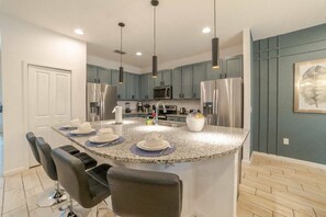 A modern kitchen with granite countertops, stainless steel appliances, and pendant lighting. - 8BR Themed Home Near Disney Pool & Game Room (Kissimmee)