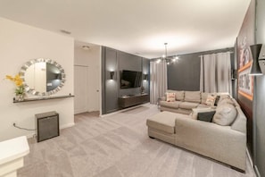 A modern living room with a sofa, TV, and a decorative mirror. - 8BR Themed Home Near Disney Pool & Game Room (Kissimmee)