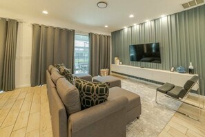Una sala moderna con un sofá seccional, un televisor de pantalla plana montado en la pared y una mesita con objetos decorativos.
